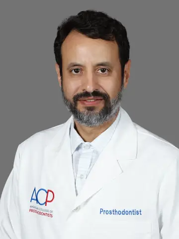 Studio portrait of Dr. Roy Rosado in a white coat embroidered with the word Prosthodontist